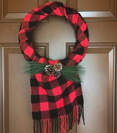 a red and black plaid christmas wreath hanging on the front door with pine cone decoration