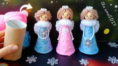 a hand is holding an item in front of three small dolls with pink hair and blue dresses