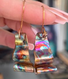 a pair of earrings that have been made out of metal and are being held by someone's hand