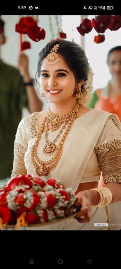 a woman in a white sari holding a bouquet of flowers and smiling at the camera