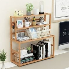 a wooden shelf filled with books next to a computer monitor and plant on top of a desk