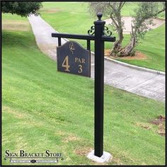 a black and gold sign on a pole in the grass next to a sidewalk with trees