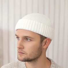 a man wearing a white hat and sweater looking off to the side in front of a striped wall