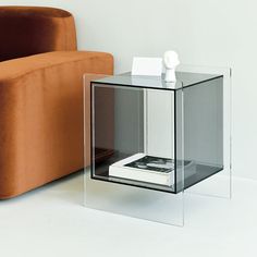 a glass table sitting next to a couch in a living room with an orange chair