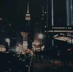 a city street at night with people walking on the sidewalk and tall buildings in the background