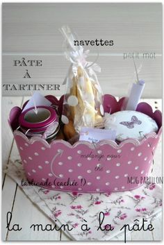 a pink polka dot basket with candles and other items in it on a white table