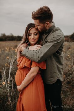 a pregnant woman hugging her husband in an open field