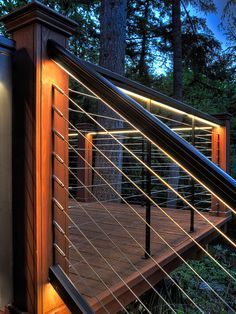 a wooden deck with metal railings and lights on the sides, surrounded by trees