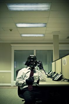 a man dressed as darth vader sitting at a desk in an office cubicle