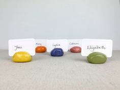 four different colored rocks sitting next to each other with name tags on the top and bottom