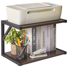 a printer sitting on top of a book shelf next to a potted plant and books