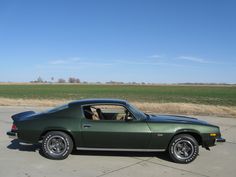 a green sports car parked in a parking lot next to an open field with grass