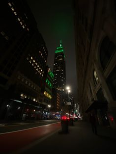 people are walking down the street at night in front of tall buildings with green lights