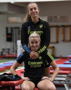 two female soccer players are posing for a photo in front of an empty gym area