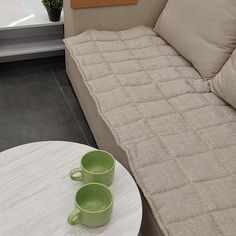 two coffee mugs are sitting on a table next to a couch with a mattress