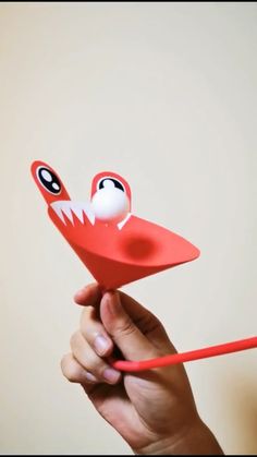 a hand holding a red origami bird with eyes on it's head