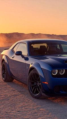 a blue sports car parked in the middle of desert at sunset with dust blowing behind it