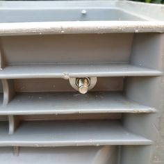 a metal shelf with three shelves and two locks on each side, in front of some bushes