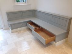 a corner bench with drawers underneath it in a room that has tile flooring and white walls