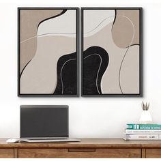 two abstract paintings on the wall above a desk with a laptop computer and stack of books