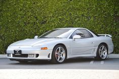 a silver sports car parked in front of a hedge