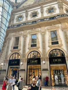 people are walking around in front of a building with many windows and glass doors on it