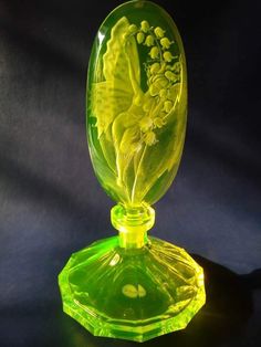 a green glass vase with flowers in it sitting on a table next to a black background