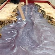 a black cat sitting on top of a wooden table next to purple liquid flowing down the floor