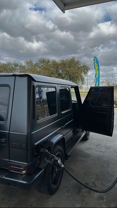 a black car is parked at a gas station with its door open and the fuel pump hooked up to it