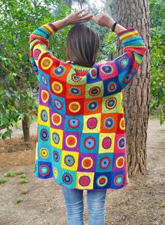 a woman standing in front of a tree wearing a colorful crocheted sweater