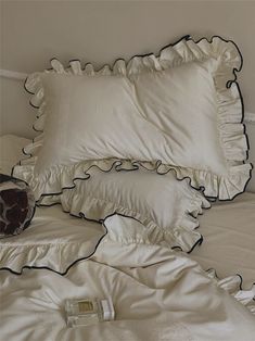 a bed with white sheets and black ruffles on the pillow cases, along with a red vase