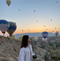 a woman standing on top of a rocky hillside next to hot air balloons in the sky