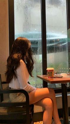 a woman sitting at a table in front of a window with rain falling down on her