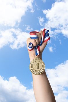 a person's hand holding up a gold medal with the number one on it