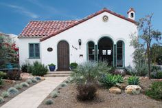 a white house with green shutters on the front and side doors is surrounded by plants