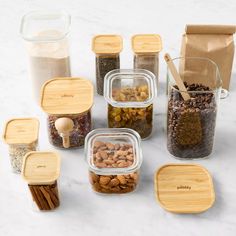 several glass containers filled with nuts and spices on a marble counter top next to wooden spoons