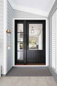 a black front door with two sidelights and blinds on the outside wall, leading to a white house