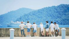 a group of people standing next to each other looking at the water and mountains in the distance