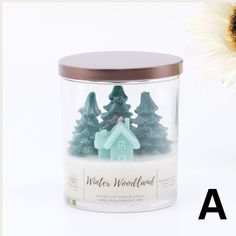 a glass jar with a house and trees in it, next to a sunflower