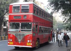 a red double decker bus driving down a street next to people walking on the sidewalk