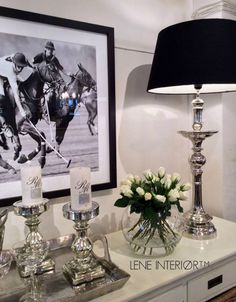 a table topped with vases filled with flowers next to a lamp and pictures on the wall