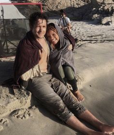 a man sitting next to a woman on top of a sandy beach in front of a tent