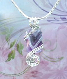 a wire wrapped necklace with a purple stone in the shape of a spiral on a floral background