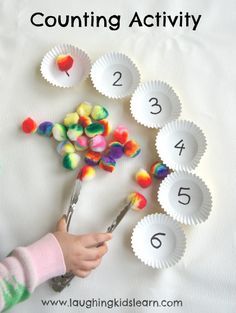 a child is holding spoons with candy in them and counting activity on the table