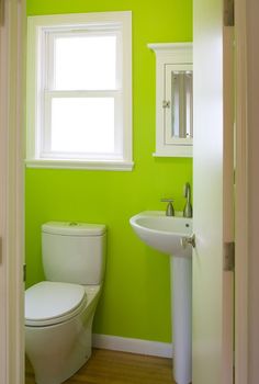 a white toilet sitting next to a bathroom sink under a window in a green room