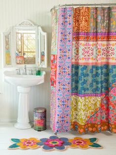 a colorful shower curtain is next to a white pedestal sink and mirror in a bathroom