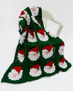 a green crocheted blanket with santa claus on it sitting on a white chair