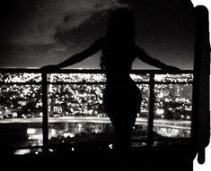 a woman standing on top of a balcony next to a night time cityscape