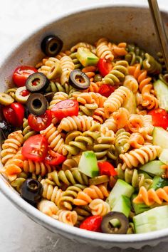 a bowl filled with pasta, olives, tomatoes and cucumber in it