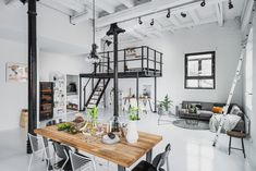 an open concept living room and dining area with white walls, exposed ceilings, black metal staircases, and wooden table